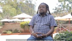 Mutemi Kiama Edwin sitting on a chair outside being interviews with trees behind him