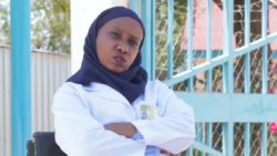 Medina Chenge sits by a gate being interviewed