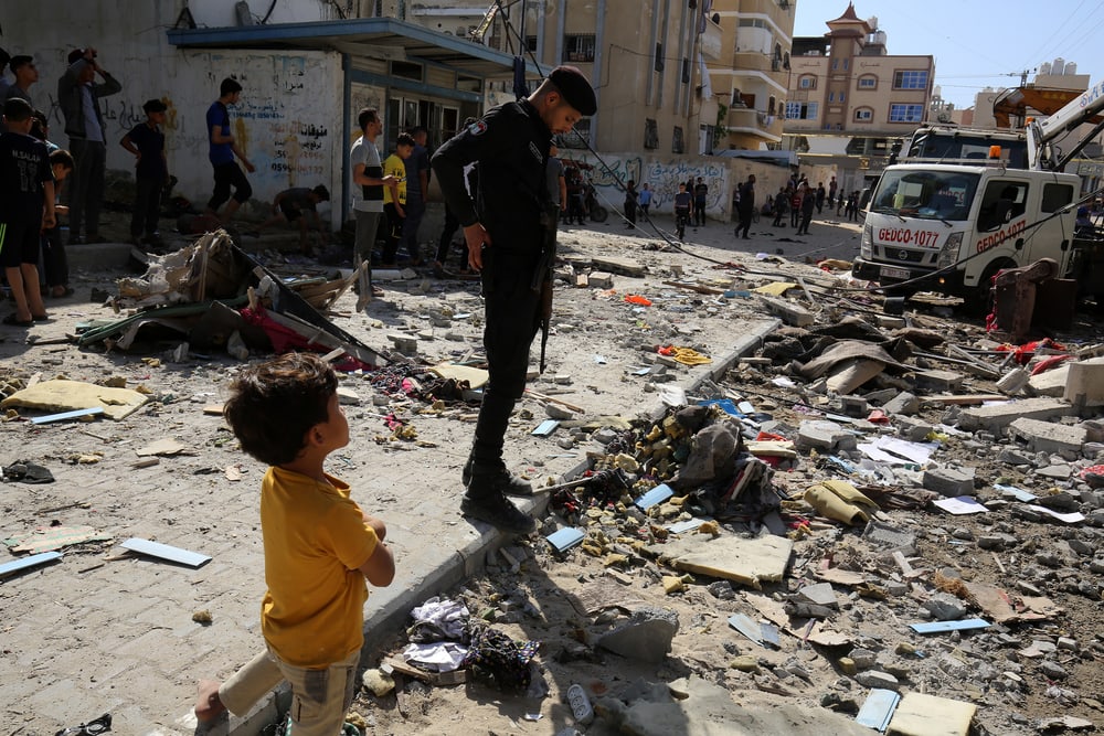 Young child and older man inspect damage caused by an Israeli air strike.